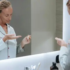 Kobieta w piżamie aplikuje na dłoń serum, które może być maścią na wypryski.