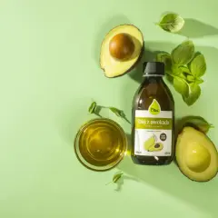 Odkryj niezwykłe olej z awokado właściwości. Butelka oleju, połówki awokado i listki bazylii na zielonym tle.