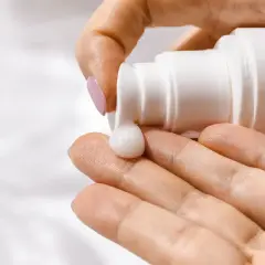 Krem z ethylhexylglycerin spływa z białej buteleczki na dłoń, tworząc gładką kroplę.