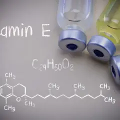 Wzór chemiczny tokoferolu, czyli witaminy E, obok fiolek z płynem.