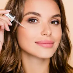 Kobieta aplikuje serum z pipetki na twarz. To może być retinol, składnik odmładzający skórę.