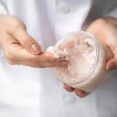 Dłonie w białym kitlu pobierają peeling z mocznikiem. Czy urea to nawilżający składnik? Tak!
