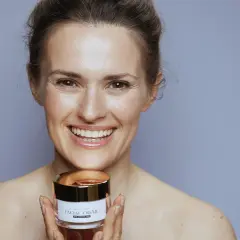 Uśmiechnięta kobieta trzyma słoiczek kremu z peptydami kolagenowymi.