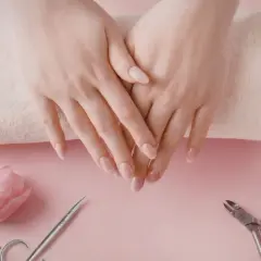 Delikatne dłonie po perfekcyjnym manicure kombinowanym. Obok różowy tulipan, cążki i buteleczka z płynem.