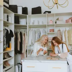 Dwie kobiety przeglądają biżuterię w garderobie. Ubrania i buty w stylu basic wiszą na wieszakach.