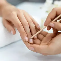 Delikatne dłonie poddawane zabiegowi manicure biologiczny. Paznokcie są naturalne, zadbane, a skórki delikatnie odsuwane patyczkiem.