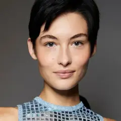 Kobieta z krótkimi, czarnymi włosami w stylu pixie bob fryzura, w błyszczącej, niebieskiej bluzce.