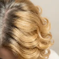 Widoczne ciemne odrosty na blond włosach, które wymagają odświeżenia koloru.