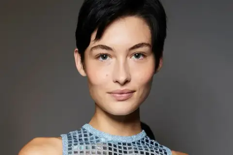 Kobieta z krótkimi, czarnymi włosami w stylu pixie bob fryzura, w błyszczącej, niebieskiej bluzce.