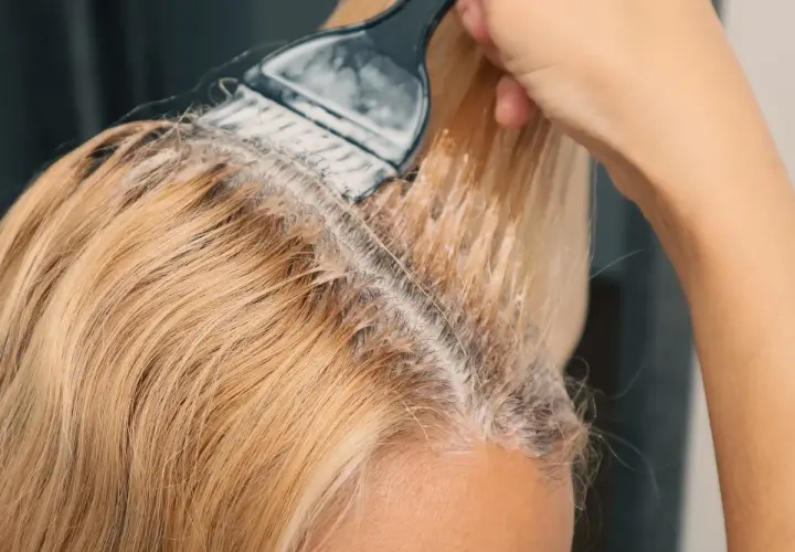 Dłoń z pędzlem nakłada produkt do rozjaśniania włosów na blond pasma.