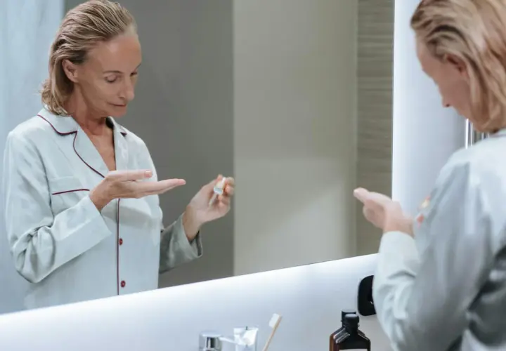 Kobieta w piżamie aplikuje na dłoń serum, które może być maścią na wypryski.