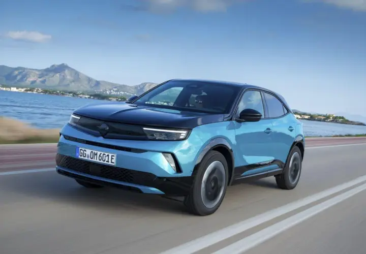 Niebieski Opel Mokka z czarnym dachem jedzie wzdłuż wybrzeża. Kolor mokka idealnie pasowałby do tej scenerii.