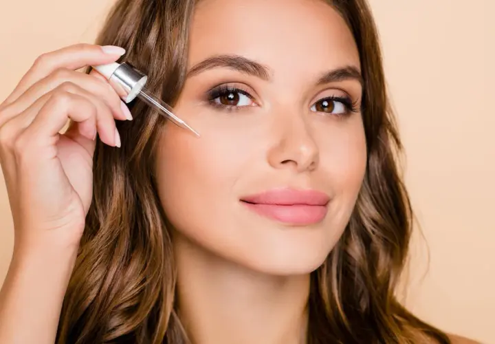 Kobieta aplikuje serum z pipetki na twarz. To może być retinol, składnik odmładzający skórę.