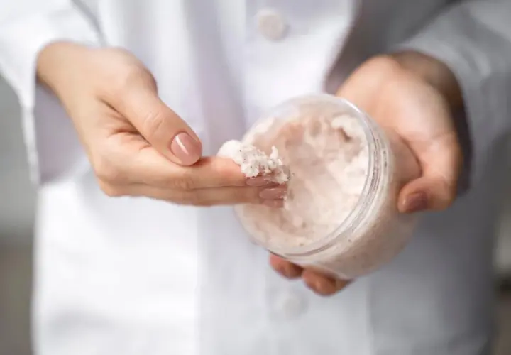 Dłonie w białym kitlu pobierają peeling z mocznikiem. Czy urea to nawilżający składnik? Tak!