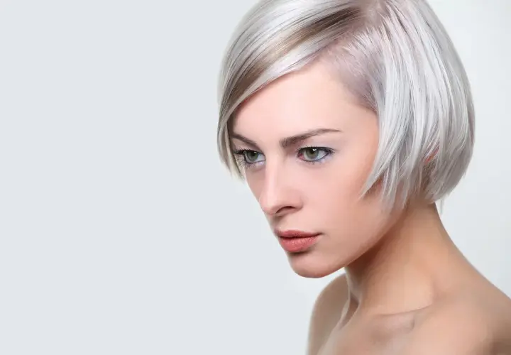 Kobieta z platynowym blond włosami, ułożonymi w nowoczesną fryzurę na pazia, z subtelnym makijażem.