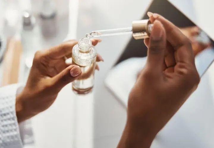 Dłonie trzymają buteleczkę z serum. Pipeta z kwasem ferulowym nabiera kroplę produktu.