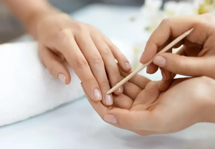 Delikatne dłonie poddawane zabiegowi manicure biologiczny. Paznokcie są naturalne, zadbane, a skórki delikatnie odsuwane patyczkiem.