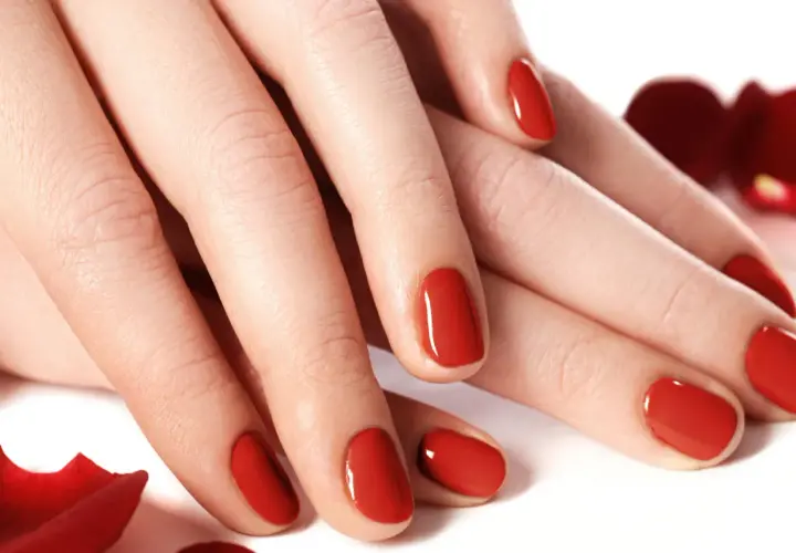 Dłonie z idealnym, czerwonym manicure. Te tytanowe paznokcie lśnią niczym drogocenne kamienie, otoczone płatkami czerwonych róż.
