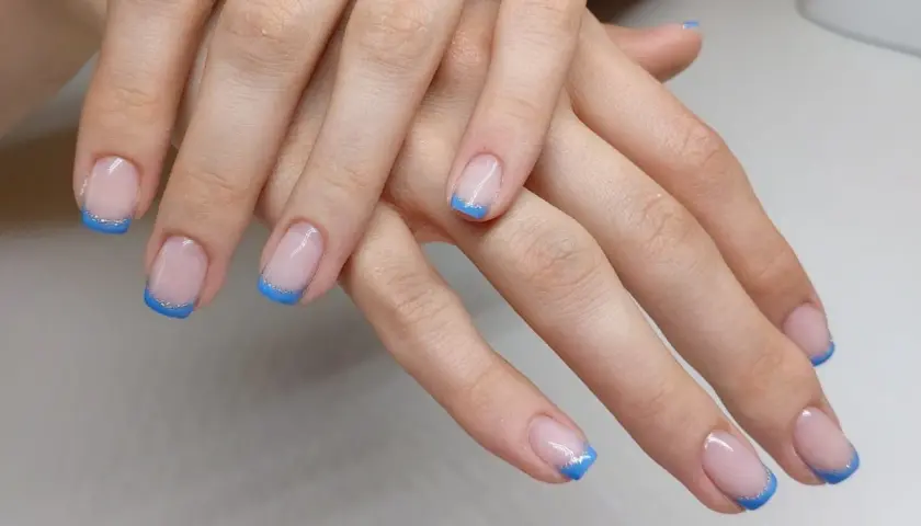 Elegancki niebieski french z brokatową linią na paznokciach.