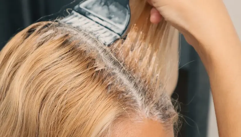 Dłoń z pędzlem nakłada produkt do rozjaśniania włosów na blond pasma.