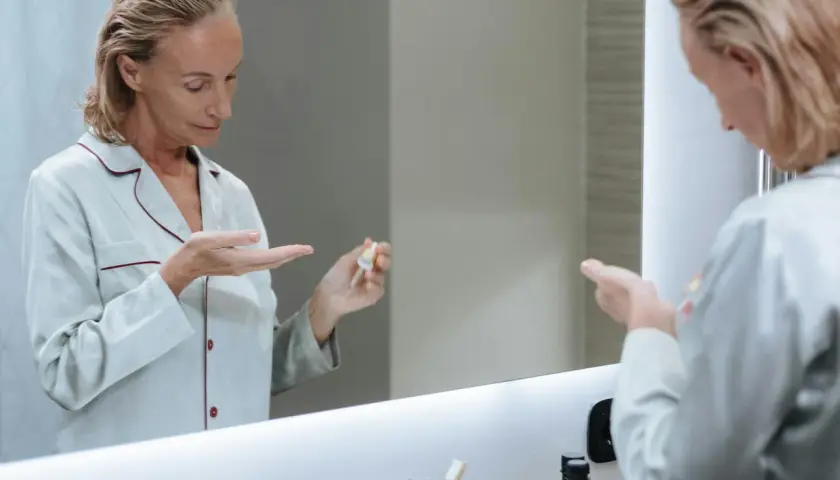 Kobieta w piżamie aplikuje na dłoń serum, które może być maścią na wypryski.