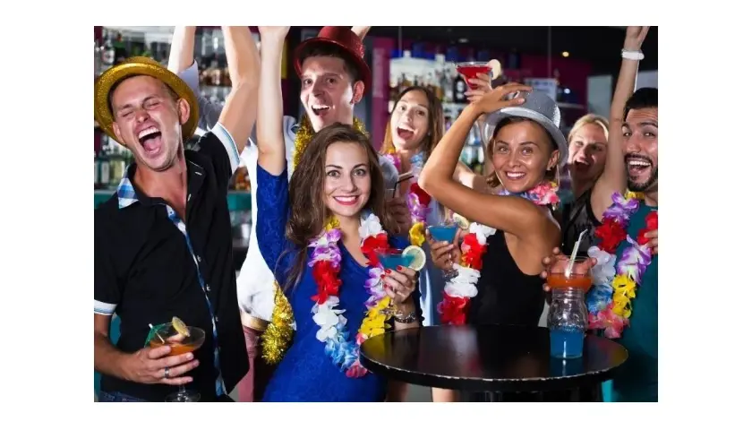 Grupa przyjaciół świętuje w stylu hawajskim, nosząc kolorowe girlandy i pijąc drinki.