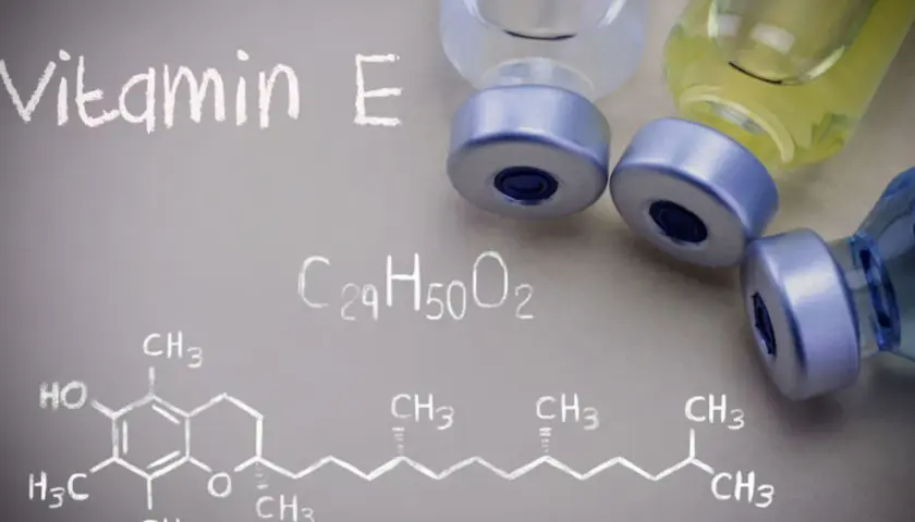 Wzór chemiczny tokoferolu, czyli witaminy E, obok fiolek z płynem.