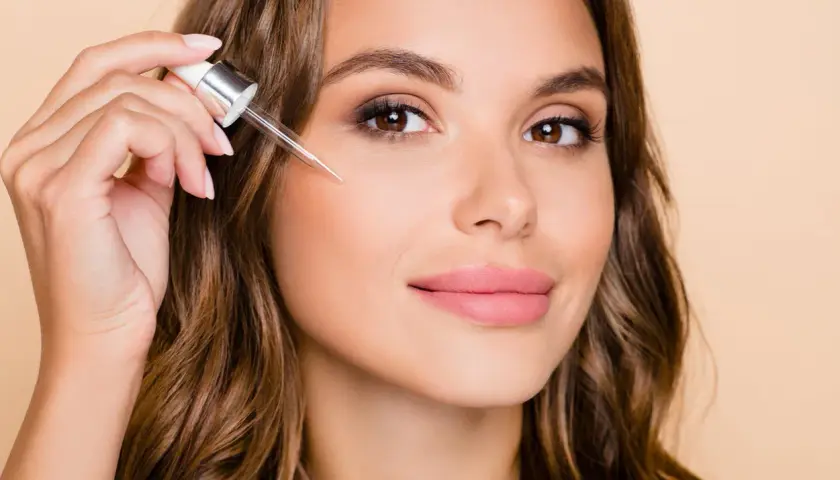 Kobieta aplikuje serum z pipetki na twarz. To może być retinol, składnik odmładzający skórę.