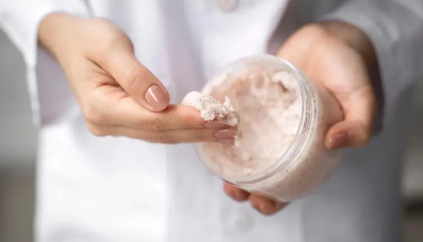 Dłonie w białym kitlu pobierają peeling z mocznikiem. Czy urea to nawilżający składnik? Tak!