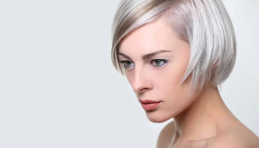 Kobieta z platynowym blond włosami, ułożonymi w nowoczesną fryzurę na pazia, z subtelnym makijażem.