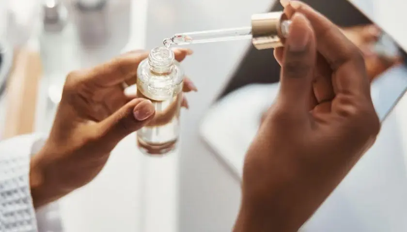 Dłonie trzymają buteleczkę z serum. Pipeta z kwasem ferulowym nabiera kroplę produktu.