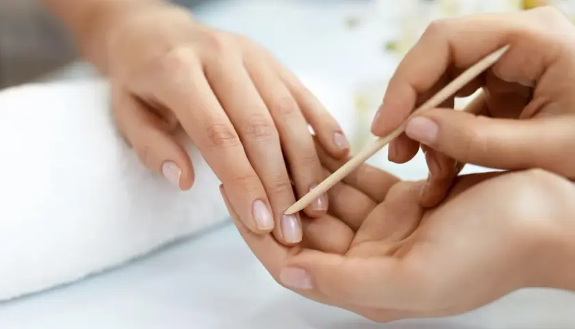Delikatne dłonie poddawane zabiegowi manicure biologiczny. Paznokcie są naturalne, zadbane, a skórki delikatnie odsuwane patyczkiem.