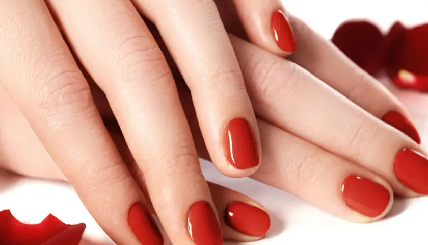 Dłonie z idealnym, czerwonym manicure. Te tytanowe paznokcie lśnią niczym drogocenne kamienie, otoczone płatkami czerwonych róż.