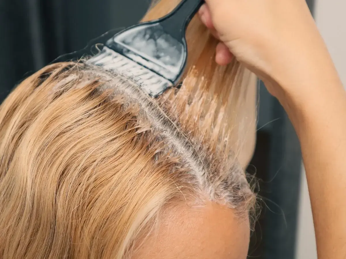 Dłoń z pędzlem nakłada produkt do rozjaśniania włosów na blond pasma.