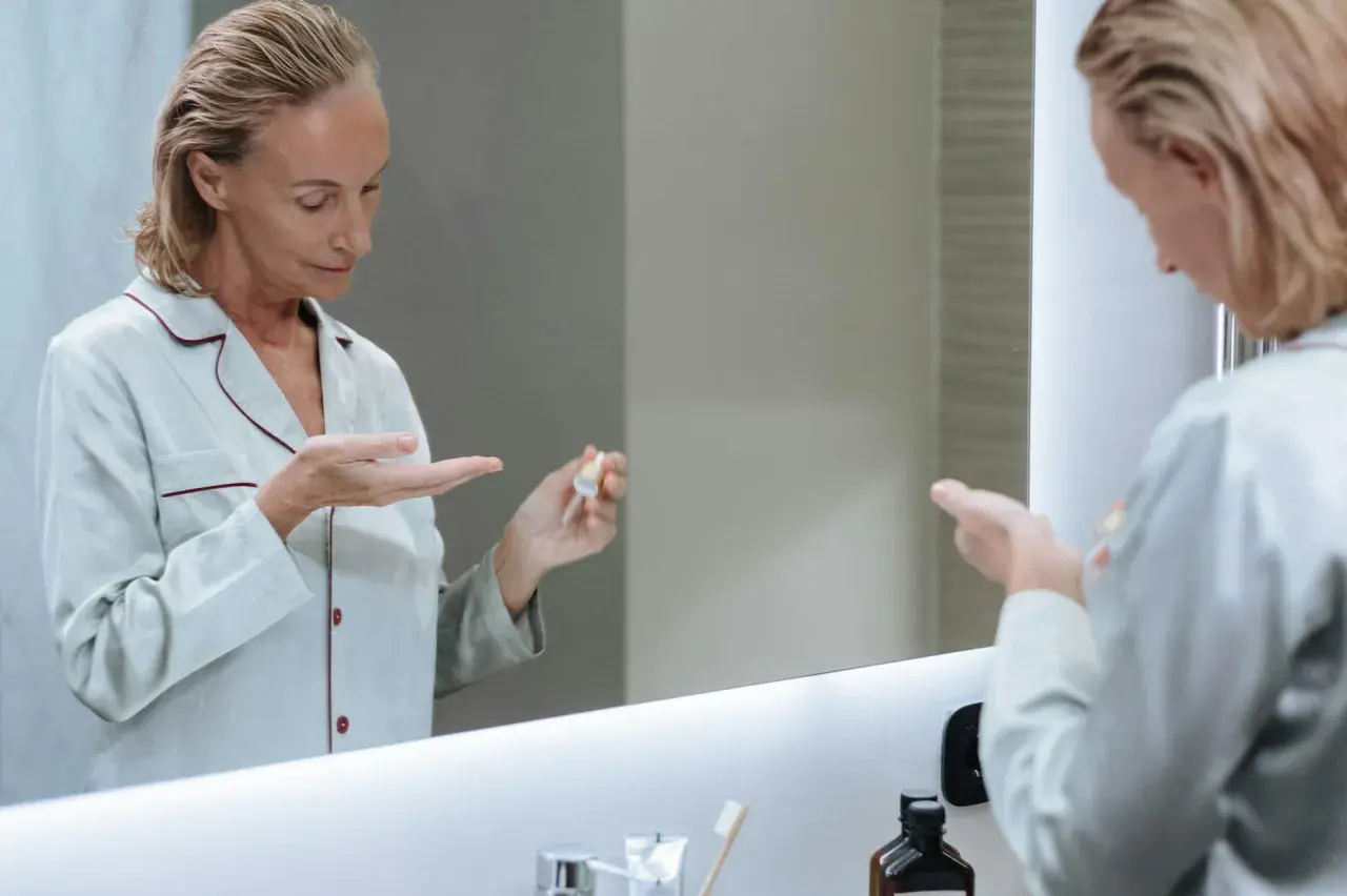 Kobieta w piżamie aplikuje na dłoń serum, które może być maścią na wypryski.