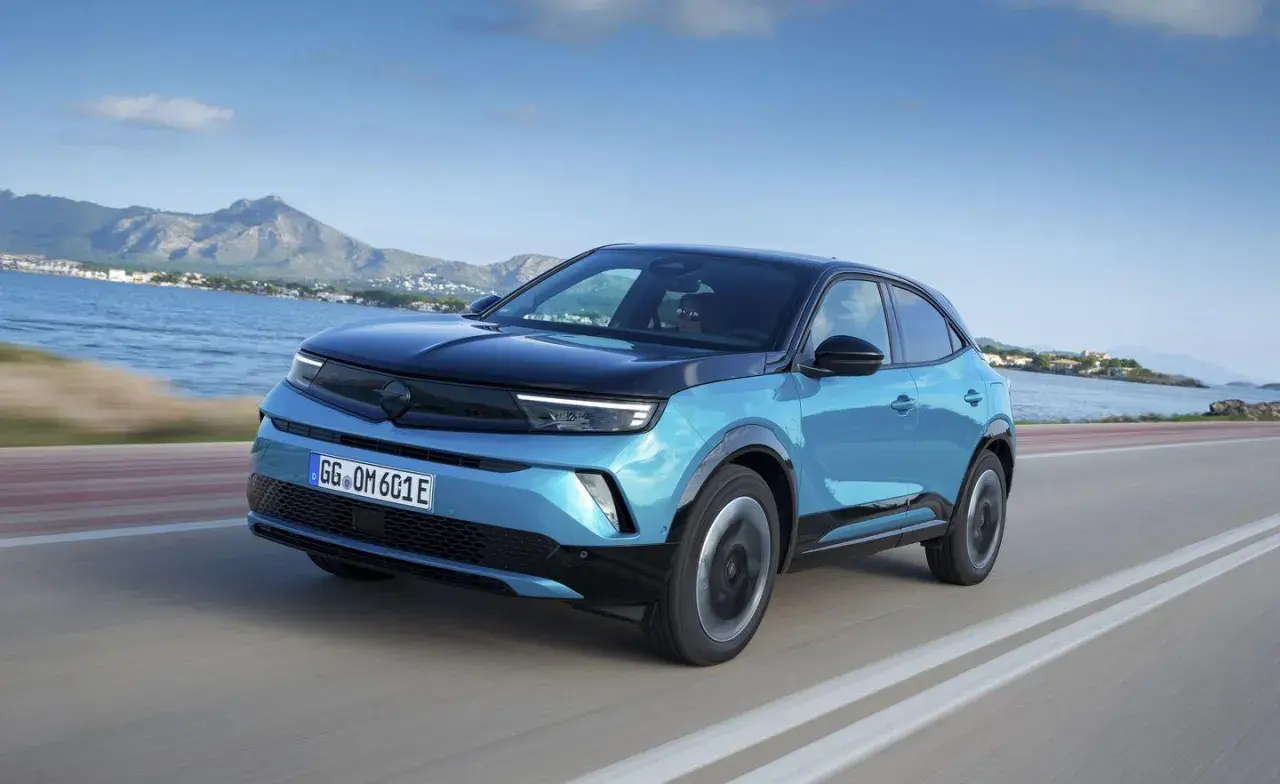 Niebieski Opel Mokka z czarnym dachem jedzie wzdłuż wybrzeża. Kolor mokka idealnie pasowałby do tej scenerii.