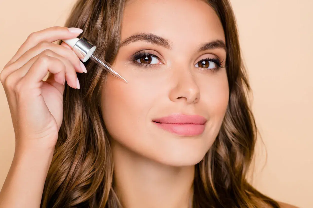 Kobieta aplikuje serum z pipetki na twarz. To może być retinol, składnik odmładzający skórę.