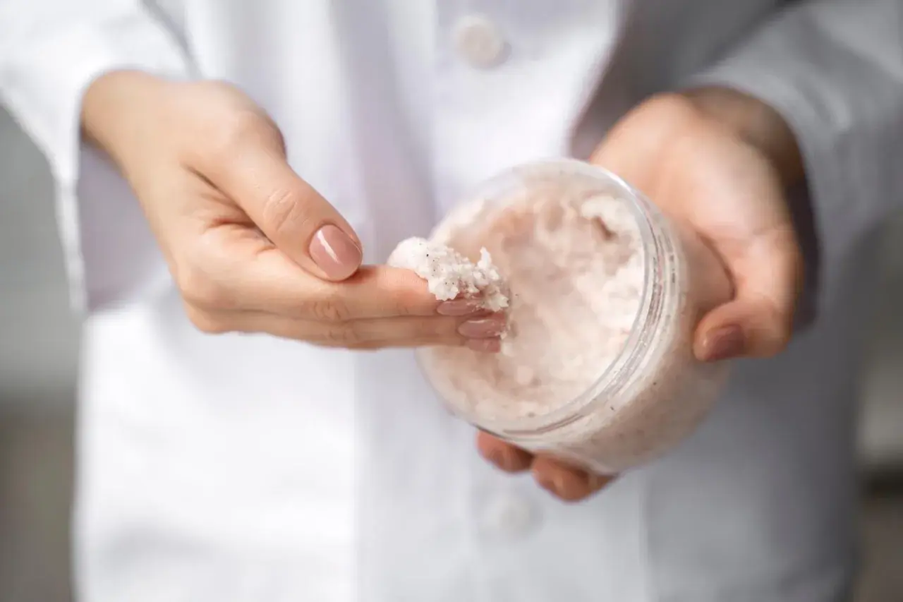Dłonie w białym kitlu pobierają peeling z mocznikiem. Czy urea to nawilżający składnik? Tak!