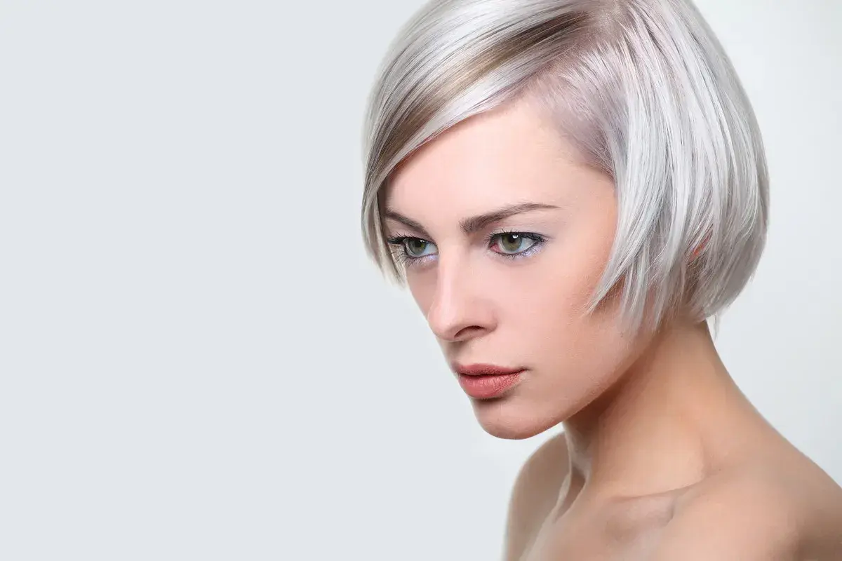 Kobieta z platynowym blond włosami, ułożonymi w nowoczesną fryzurę na pazia, z subtelnym makijażem.