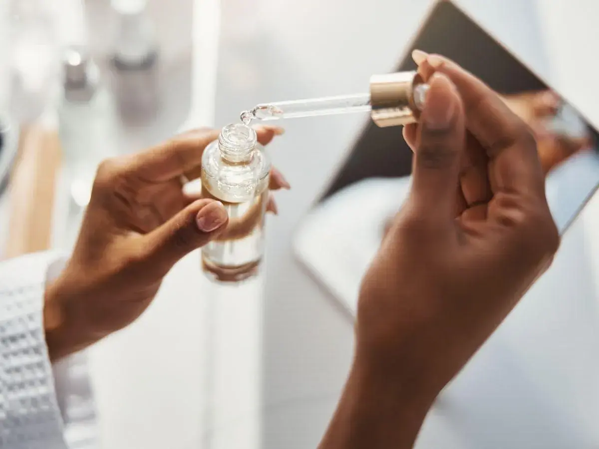 Dłonie trzymają buteleczkę z serum. Pipeta z kwasem ferulowym nabiera kroplę produktu.