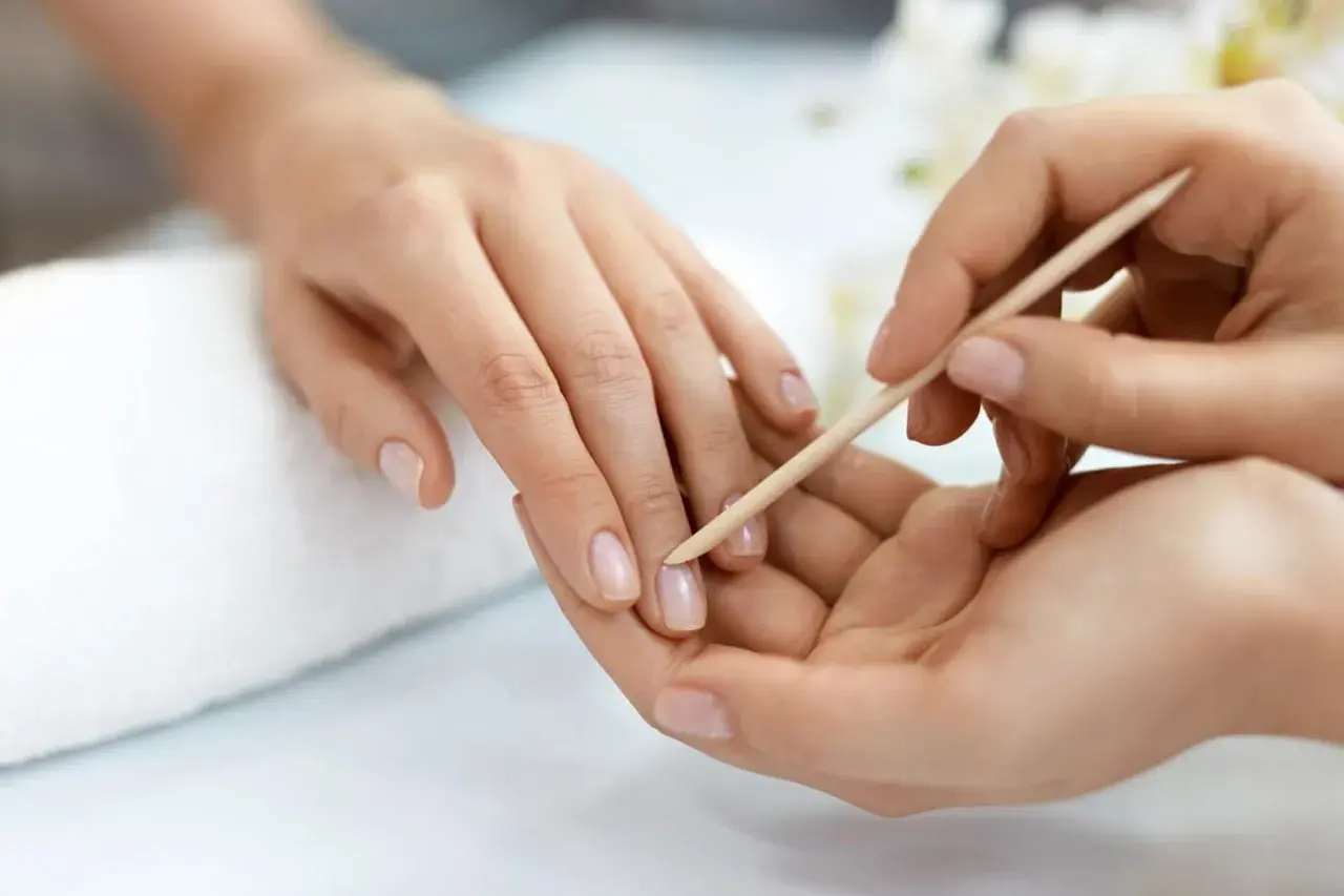 Delikatne dłonie poddawane zabiegowi manicure biologiczny. Paznokcie są naturalne, zadbane, a skórki delikatnie odsuwane patyczkiem.