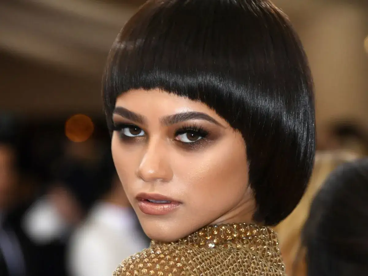 Zendaya w odważnej fryzurze na pazia, z błyszczącym złotym kołnierzem.