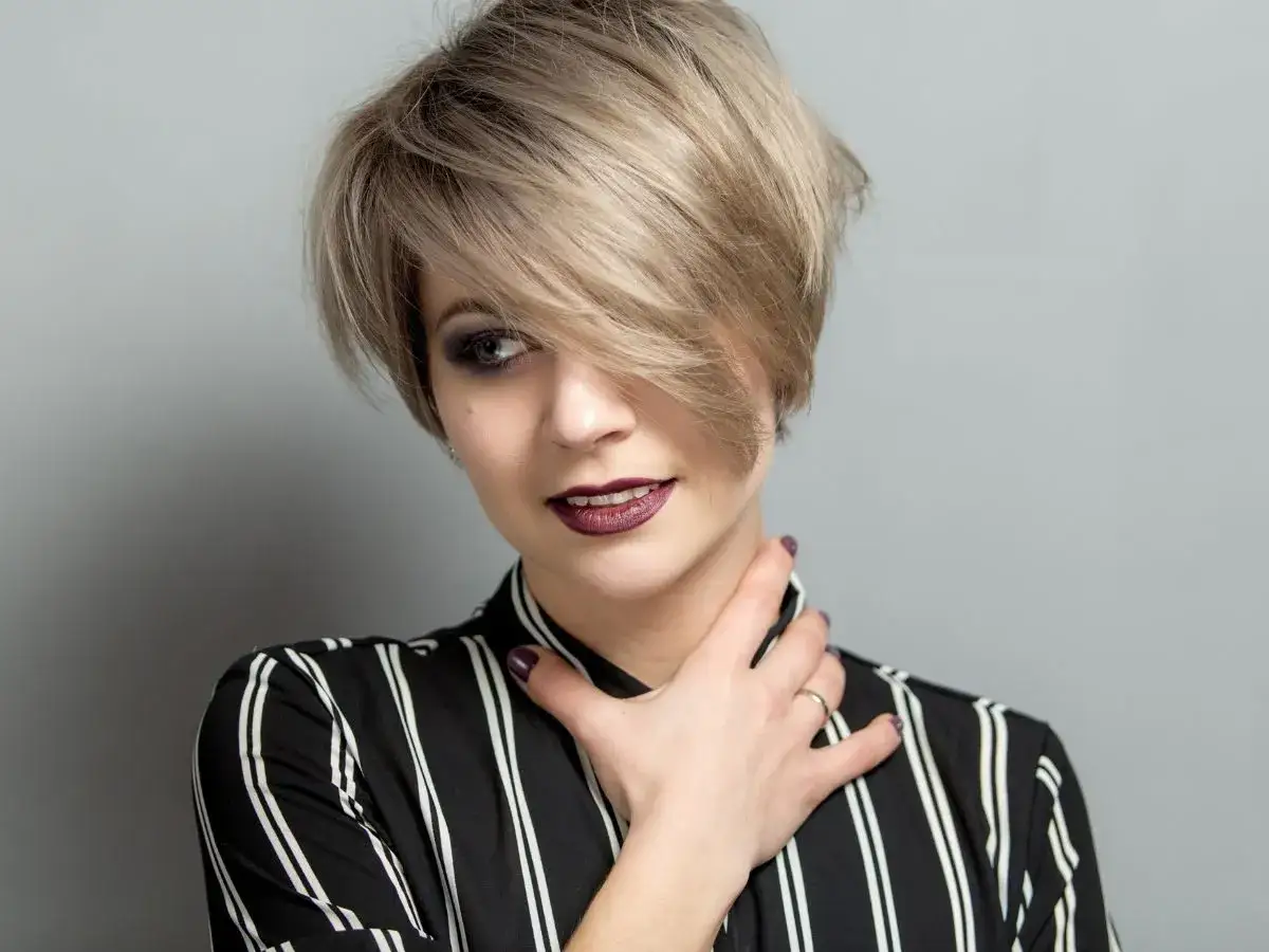 Kobieta z modną fryzurą pixie bob, w bluzce w paski, z ciemną szminką i makijażem oczu.