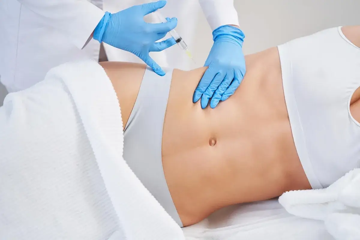 Zabieg liposukcji kawitacyjnej brzucha. Dłoń w niebieskiej rękawiczce z igłą wstrzykuje preparat.